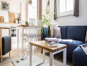 Una sala de estar moderna con un sofá, una mesa de centro de madera, un comedor con sillas y una cocina al fondo.