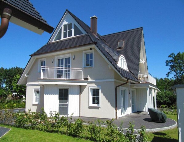 Une maison à deux étages avec un balcon, une cheminée et une pelouse bien entretenue.