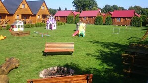 A grassy outdoor area with wooden benches, a small fire pit, and children's play structures. - Cozy Holiday Homes Near the Beach in Jaroslawiec (Postomino)