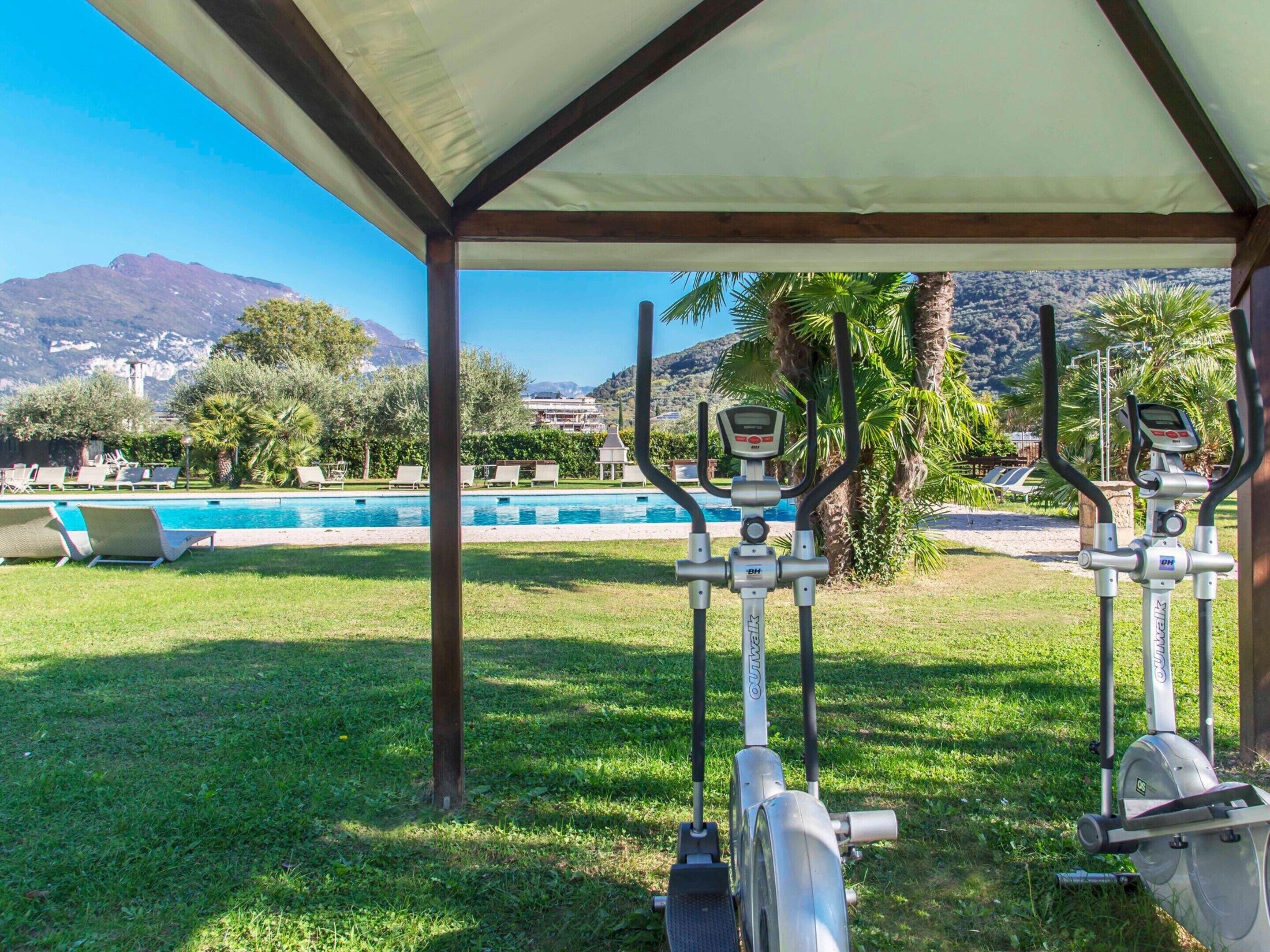 An outdoor gym area with exercise equipment, a pool, and a view of mountains and greenery.