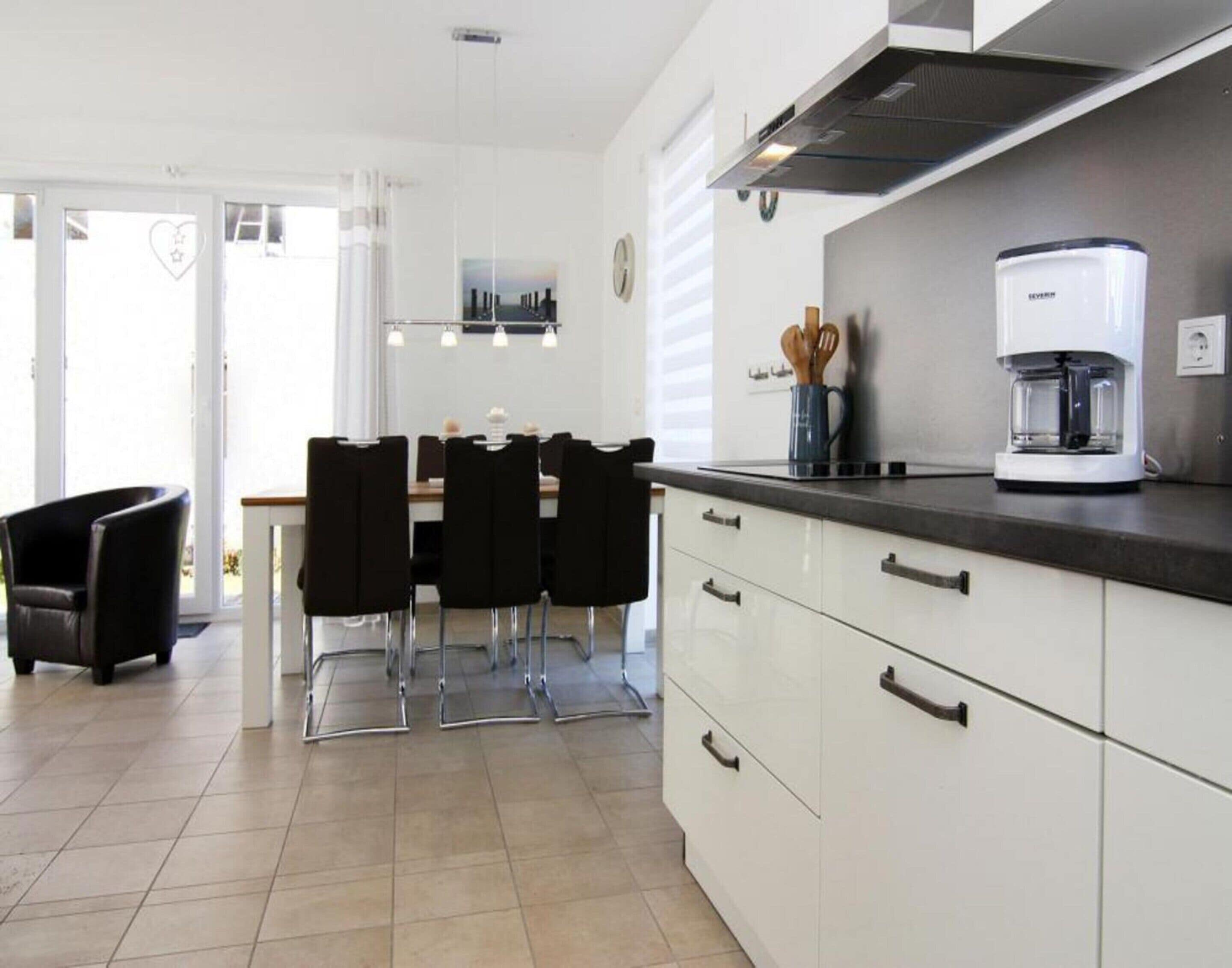 A modern kitchen with white cabinets, a coffee maker, and a dining area with black chairs.