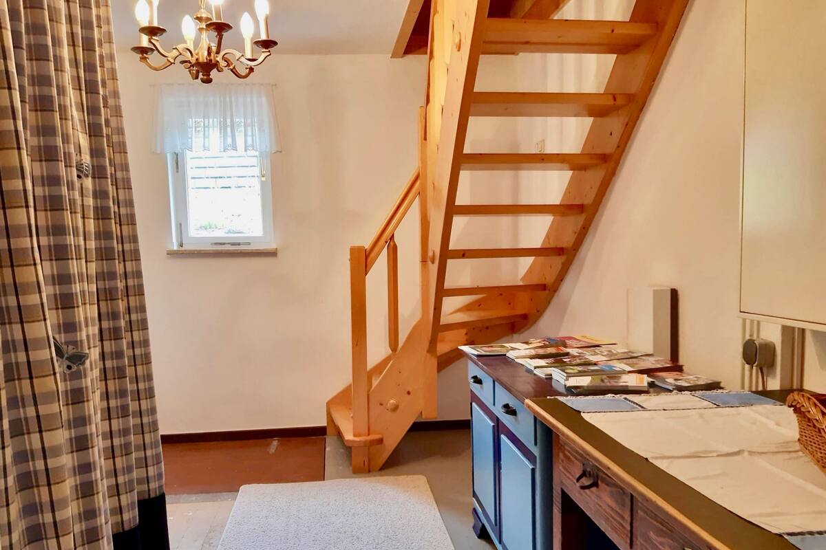 A staircase leading to an upper floor, a window with a view, a chandelier, and a desk with books and papers.