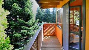 Un balcon en bois avec une porte vitrée donnant sur un espace abrité, le tout entouré d’une végétation luxuriante.