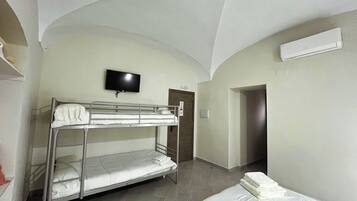 Habitación con literas, un televisor montado en la pared, una puerta y un equipo de aire acondicionado.