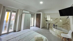 A modern bedroom with a bed, a bathroom with a bathtub, and a TV mounted on the wall. - Hostal Pompeya (Merida)