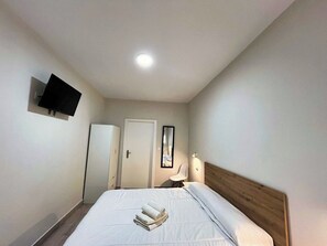 Una camera d'albergo con un letto, una televisione montata a parete, una porta e uno specchio.