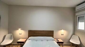 Una habitación de hotel con una cama, dos mesitas de noche, dos sillas y una ventana con persianas.