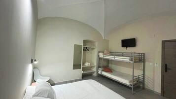Um quarto com uma cama beliche, uma mesinha de cabeceira, um espelho, um guarda-roupa e uma televisão na parede.