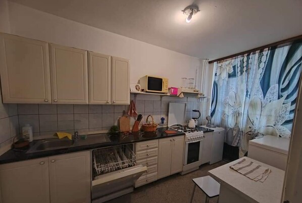 A compact kitchen with white cabinets, a microwave, a stove, and a sink. - Apartment Korzo (Bjelovar)
