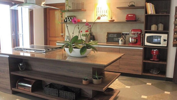 Une cuisine moderne avec un îlot central, des meubles en bois, un four à micro-ondes, une machine à café rouge et une plante en pot.