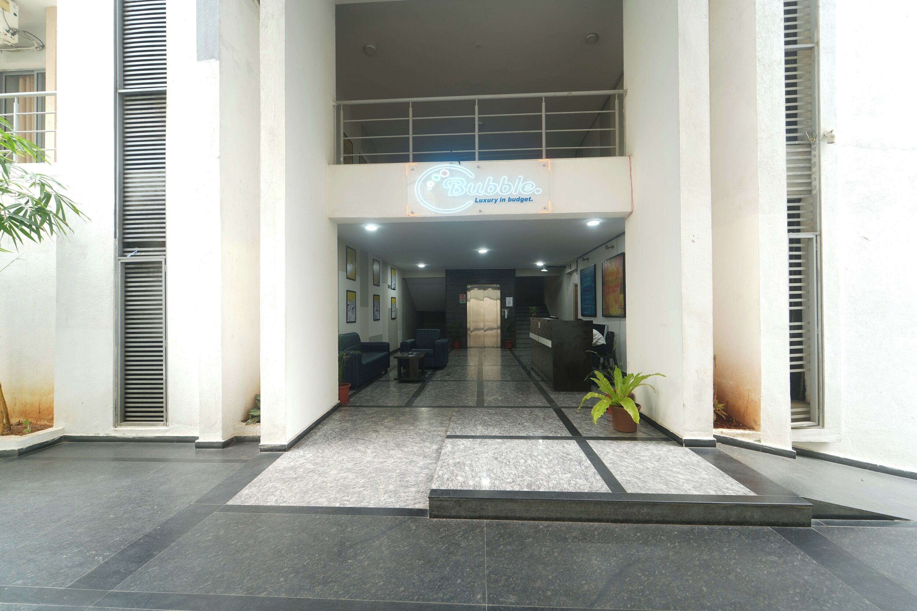 A hotel lobby with a reception desk, seating area, and a staircase leading to an upper floor.