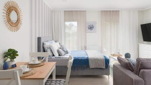 Een moderne hotelkamer met een bed, een televisie, een eethoek en een raam met gordijnen.