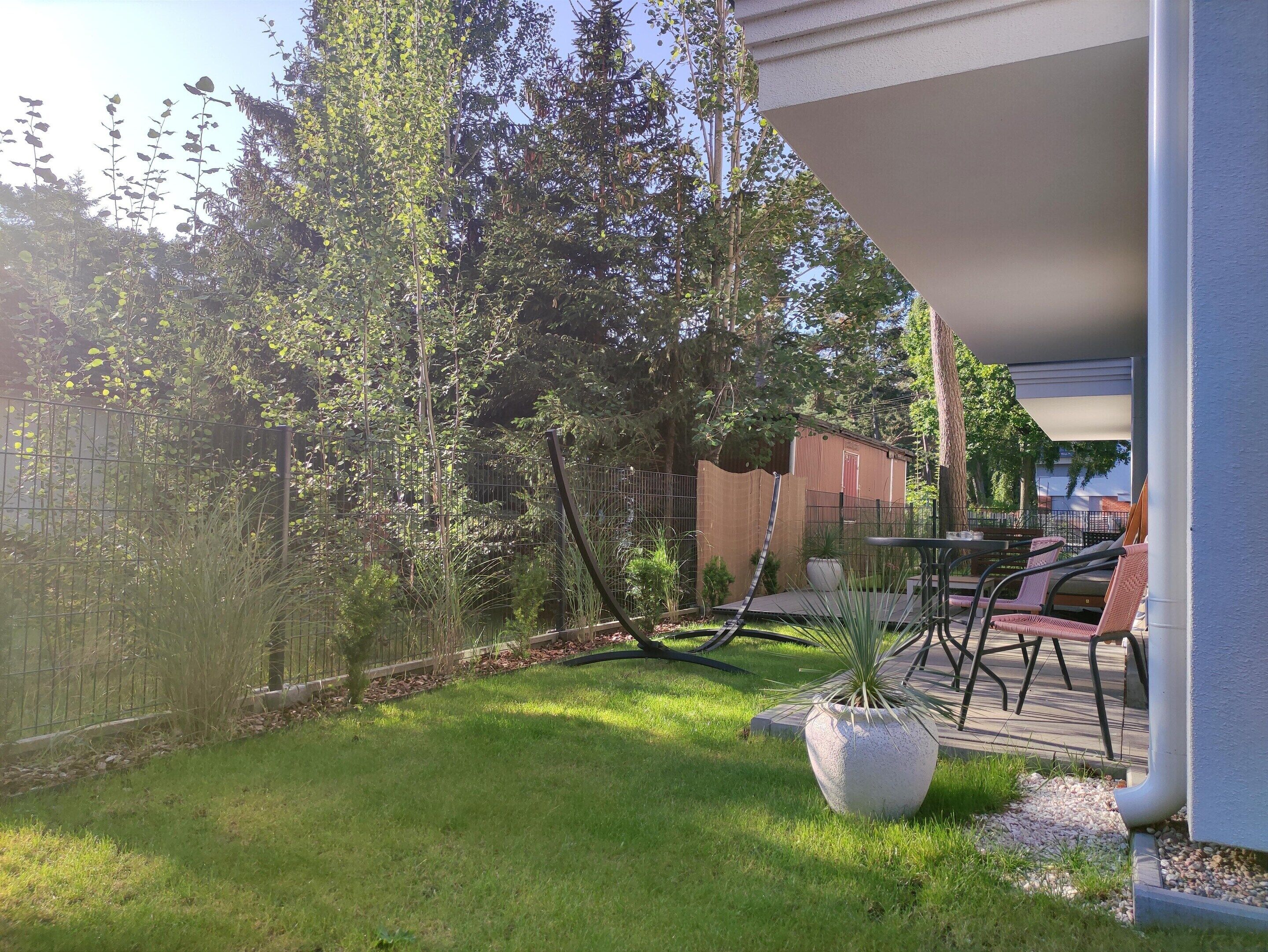 A patio area with a table and chairs, surrounded by a fence and greenery.