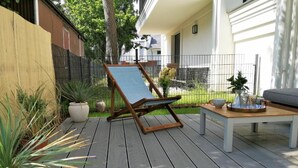 Een terras met een houten stoel, een tafeltje en potten met planten.