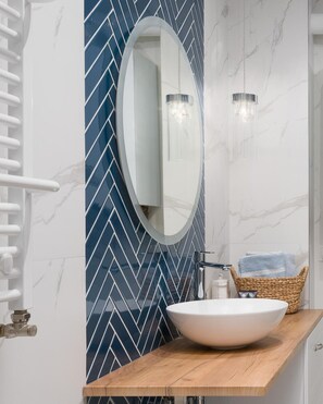 A bathroom with a white marble wall, a blue herringbone tile backsplash, a round mirror, a white vessel sink, and a wooden countertop. - A Comfortable Apartment With a Garden for 2 People, Pobierowo (Rewal)