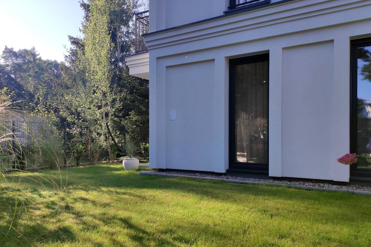 Une maison moderne dotée d’une grande porte vitrée, d’une pelouse bien entretenue et d’un jardin où poussent différentes espèces de plantes.