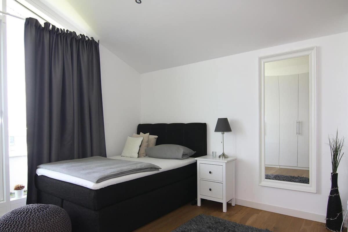 A bedroom with a bed, bedside table, lamp, and a mirror.
