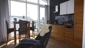 A modern living room with a sofa, a dining table with chairs, and a kitchen area with wooden cabinets and a black countertop. - Apartment House Calmsailing, Borgerende (Boergerende-Rethwisch)