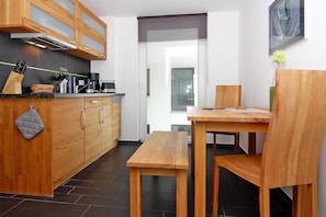 A modern kitchen with wooden cabinets, a black countertop, and a wooden dining table with chairs. - Apartment House Calmsailing, Borgerende (Boergerende-Rethwisch)