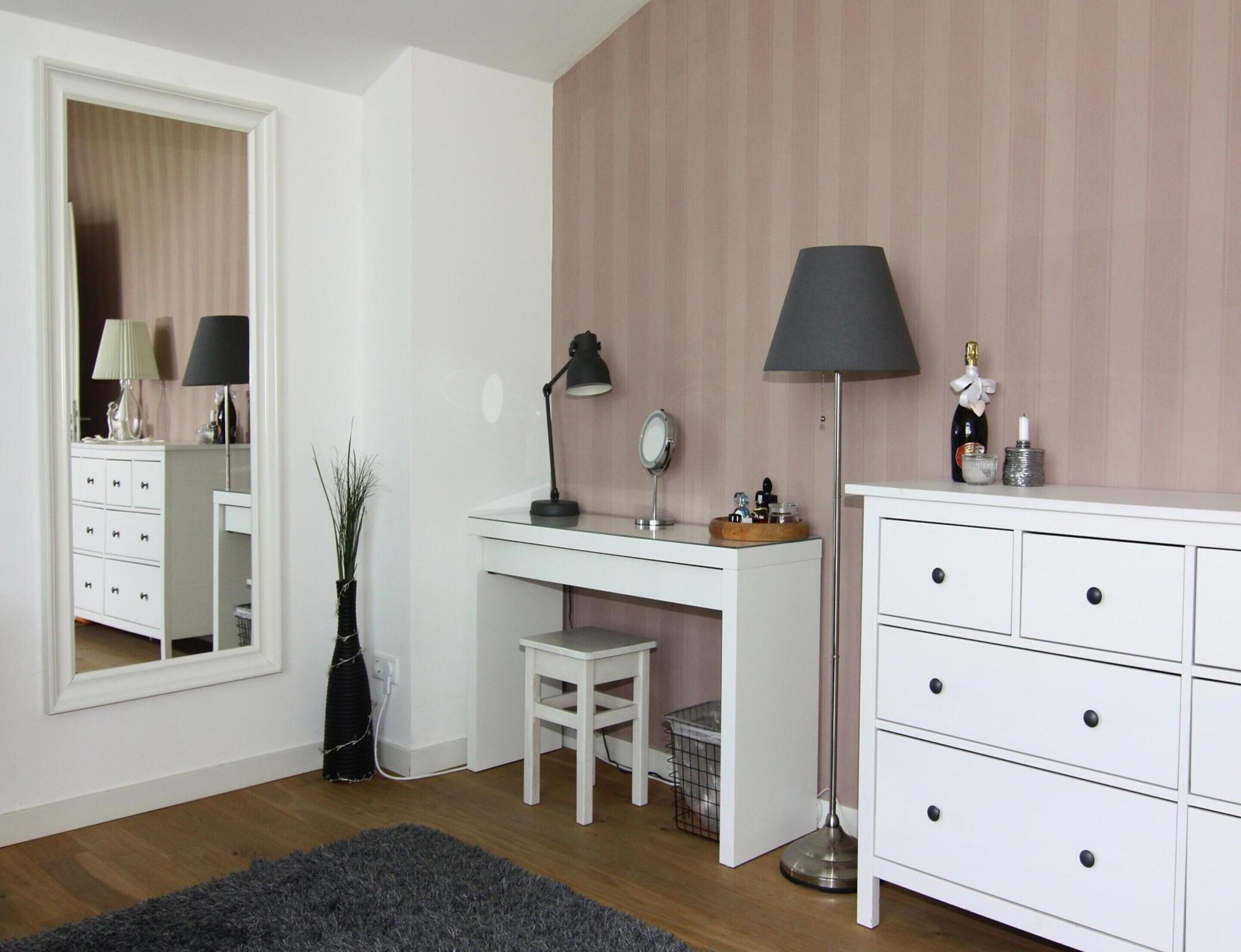 A bedroom with a white desk, a chair, a dresser, a mirror, a lamp, and a small plant.