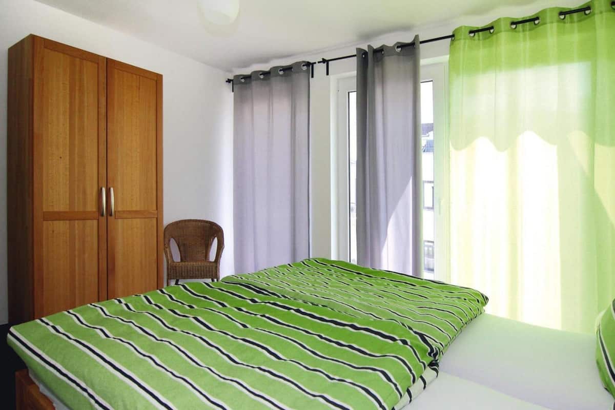 A bedroom with a bed, a wooden wardrobe, a chair, and a window with curtains.