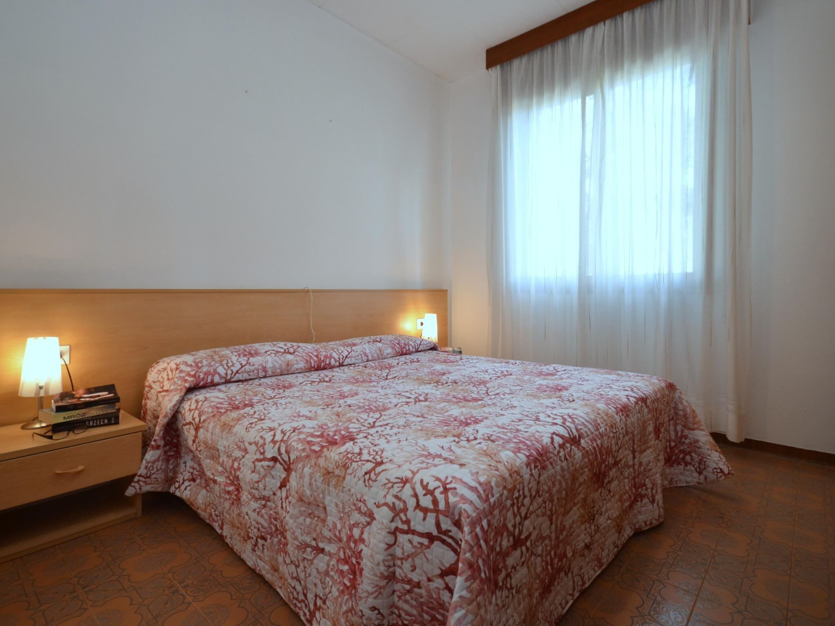 A hotel room with a large bed, a nightstand with a lamp, and a window with curtains.
