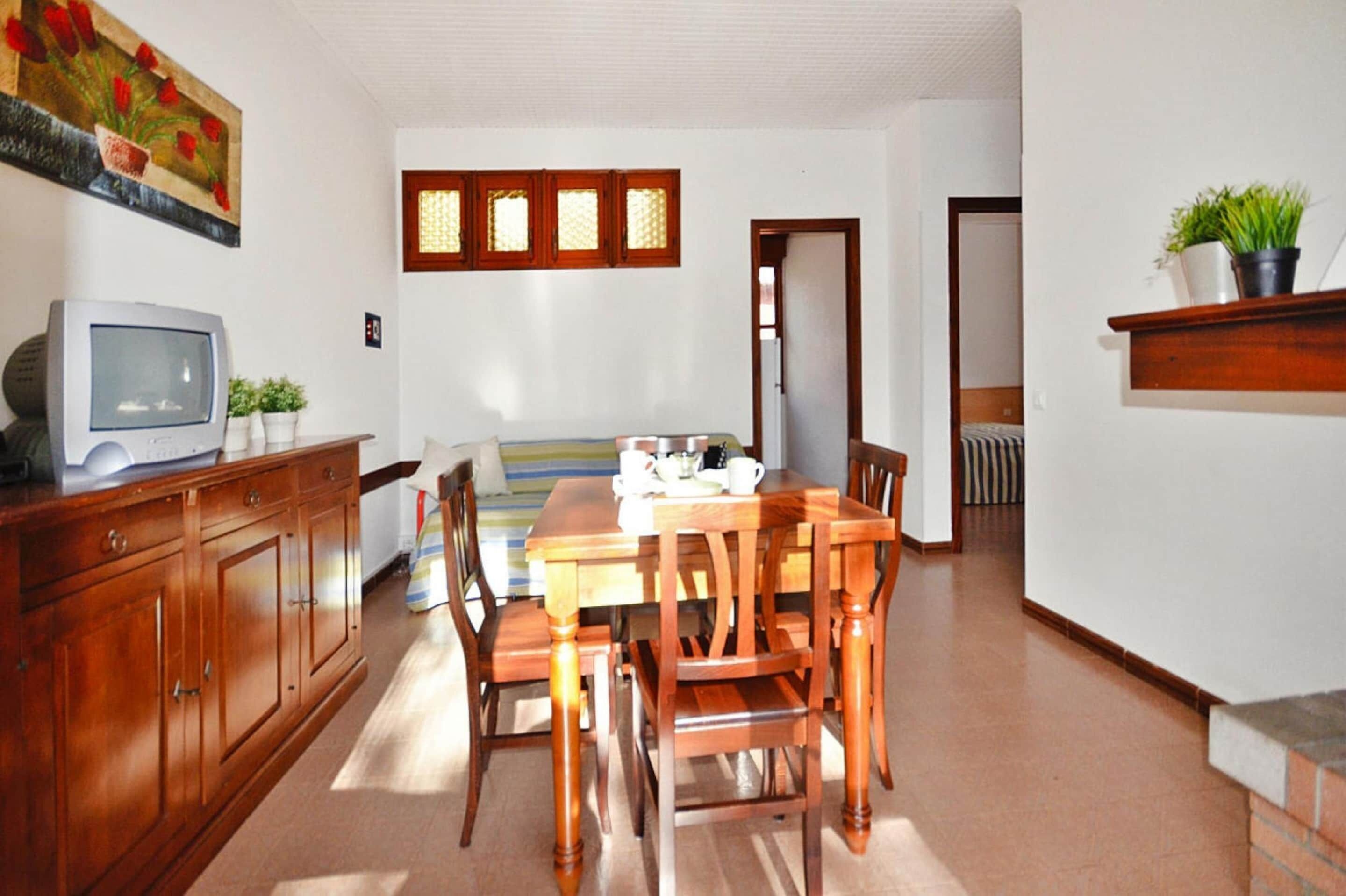 A dining area with a wooden table and chairs, a television on a cabinet, and a painting on the wall.
