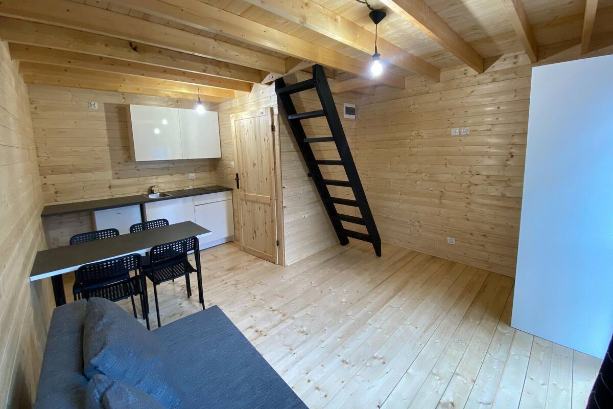 A compact wooden cabin with a kitchenette, a dining area with a table and chairs, and a loft bed.