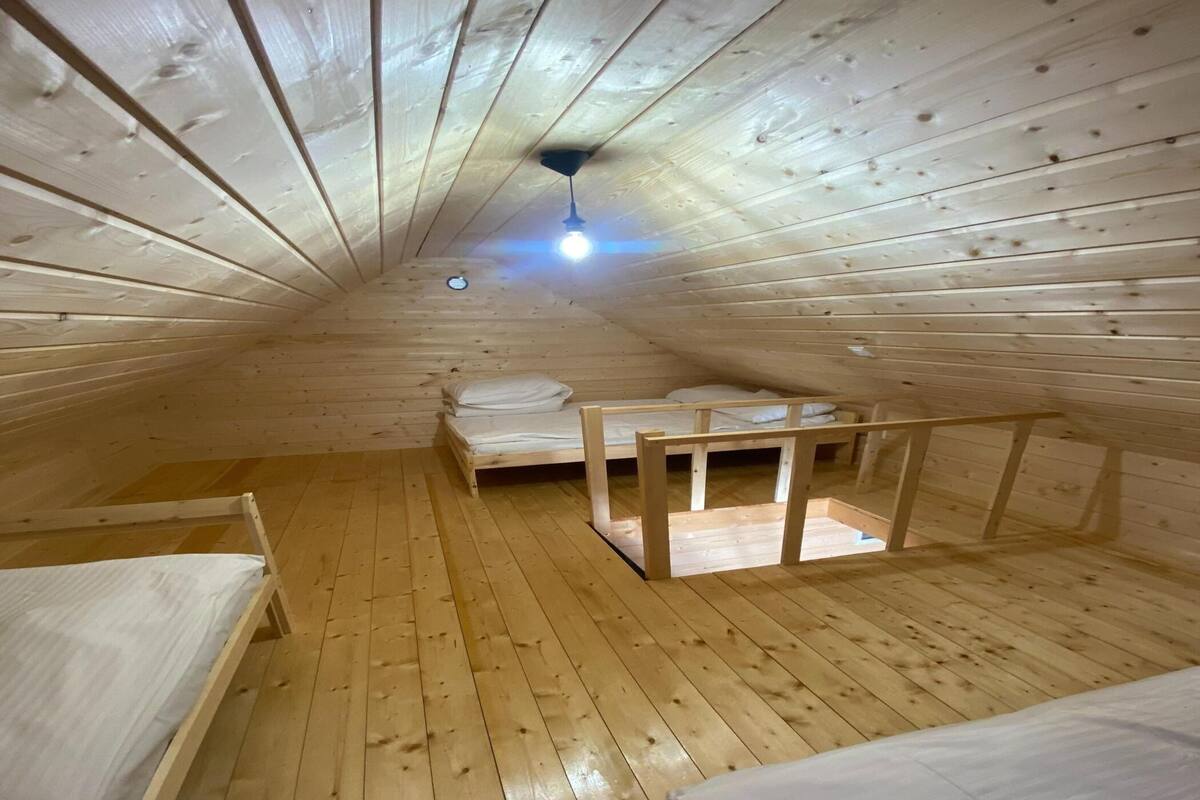 A small, wooden attic bedroom with two beds and a ceiling fan.