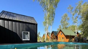 A swimming pool with a wooden cabin and a black building in the background. - Resort Pirates in Dziwnow for 4 Persons (Dziwnów)