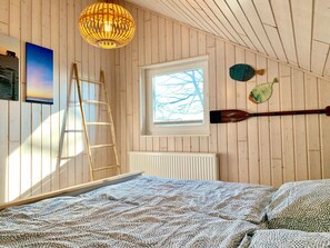 A wooden-paneled room with a bed, a ladder, a window, and a wall-mounted paddleboard. - Lovely Holiday Home in Dummer Near Lake (Dümmer)