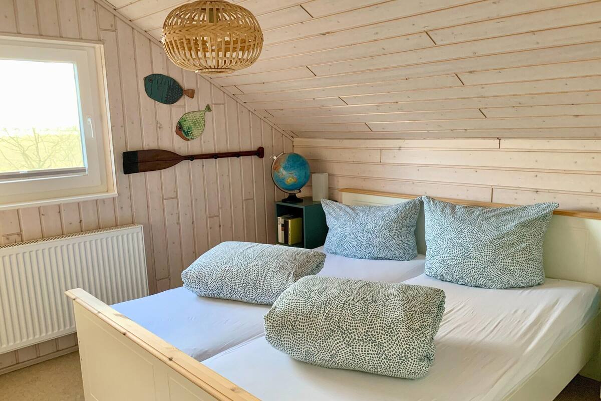 Un dormitorio con techo inclinado de madera, una cama con almohadas estampadas, un globo terráqueo y una pala en la pared.