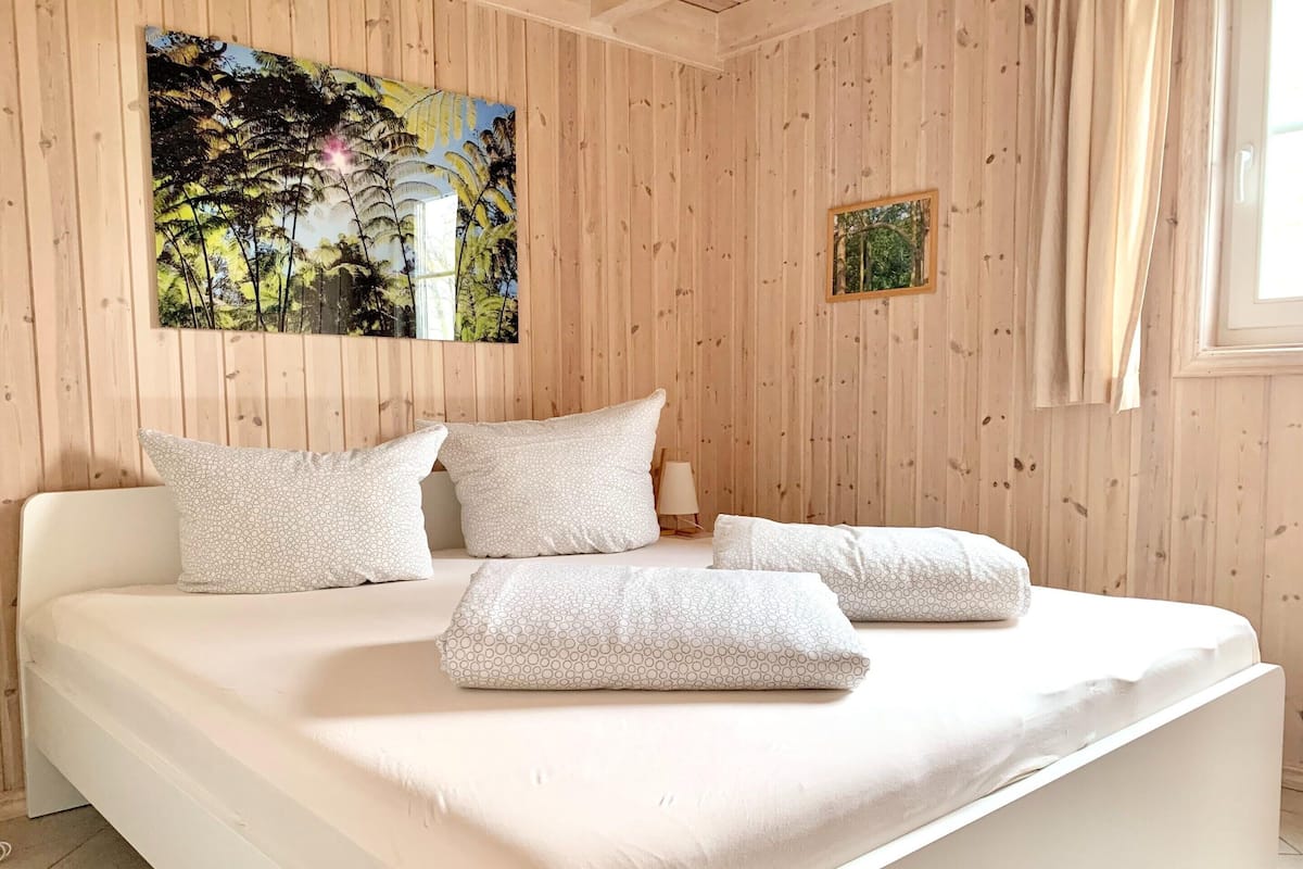 Un dormitorio con una cama grande, paredes de paneles de madera, un cuadro con árboles y una ventana pequeña.