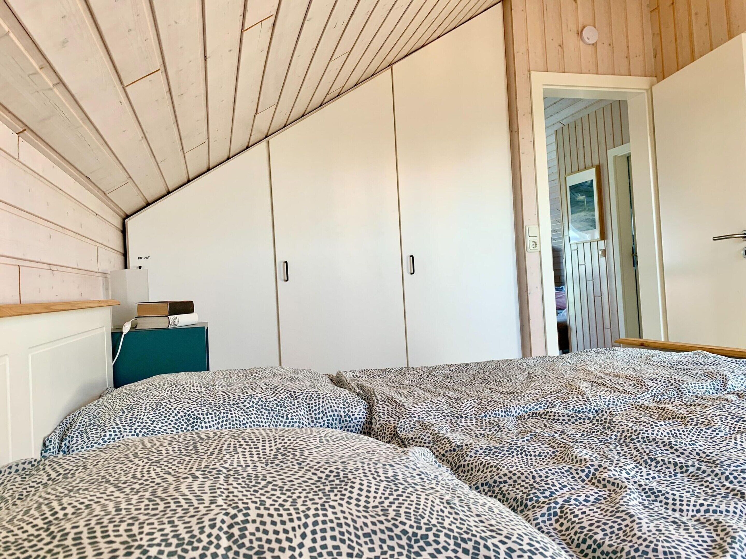 A bedroom with a sloped ceiling, a wardrobe, a bedside table with books, and patterned bedding.