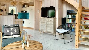 Una sala de estar acogedora con una escalera de madera, un televisor y una estantería.