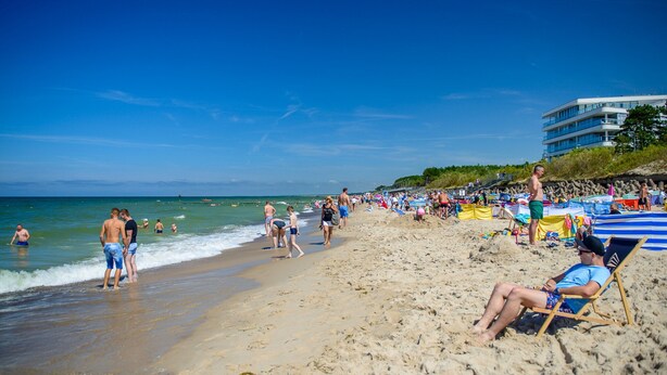A crowded beach with people walking and relaxing, a building with multiple balconies, and a clear blue sky. - Apartment With a Terrace in Mielno (Mielno)