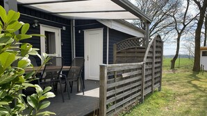 Un espace extérieur abrité, aménagé avec une table et des chaises, une clôture en bois et offrant une vue sur le paysage environnant.