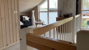 Une chambre confortable située sous les toits, avec un plafond en bois, un canapé, un vase blanc et une vue sur l’extérieur.