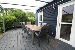 A covered patio with a wooden table and chairs, a sliding glass door, and a view of greenery. - Holiday Home Seeidyll am Dummer See, Dummer (Dummer)
