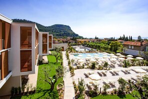 A modern hotel with a swimming pool, outdoor seating, and a view of a mountainous landscape. - Residence Olivo, Garda (Garda)