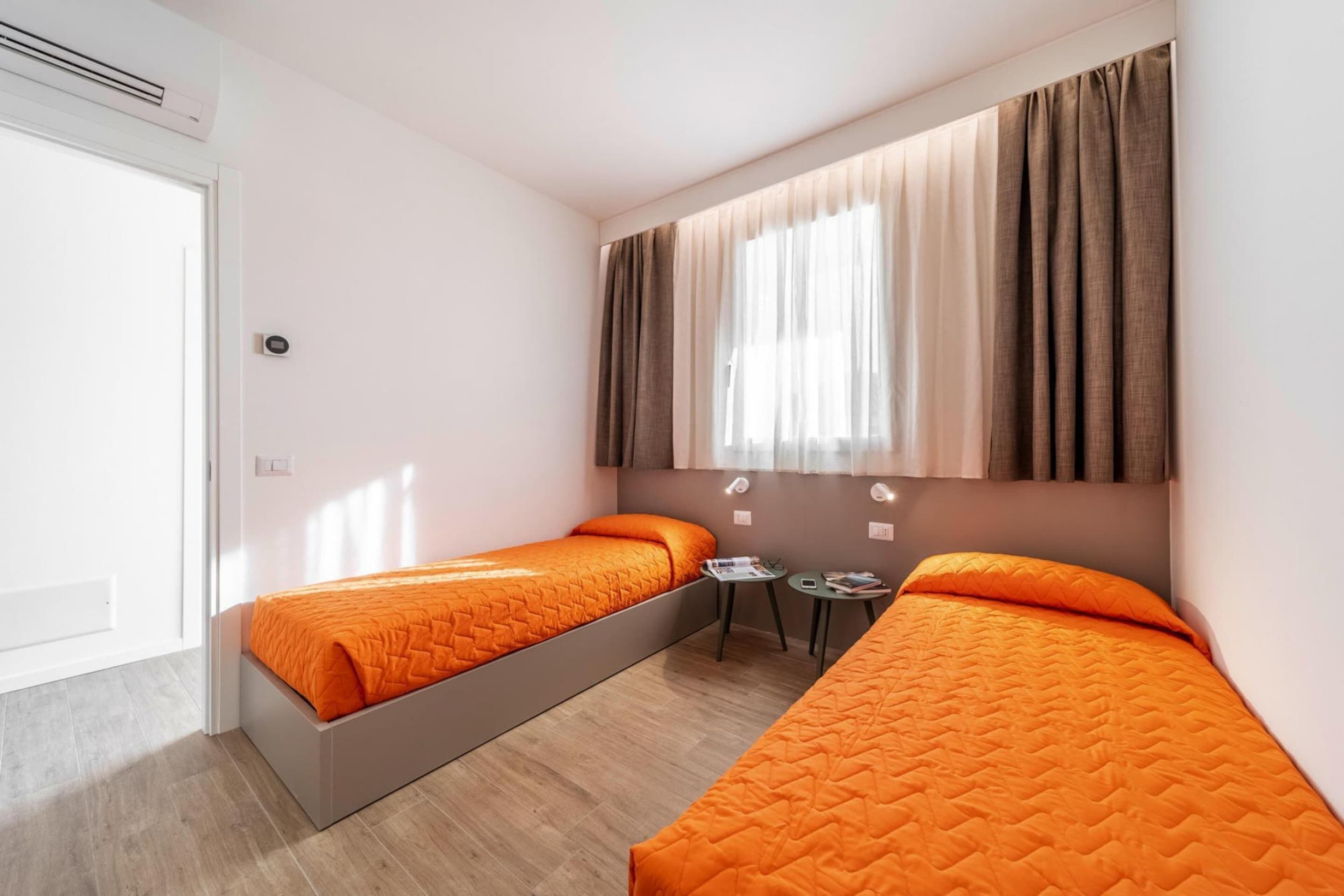 A room with two beds, a small table, and a window with curtains.