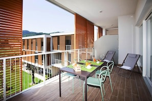 A balcony with a dining table set for two, surrounded by chairs, and a view of a building and greenery below. - Residence Olivo, Garda (Garda)