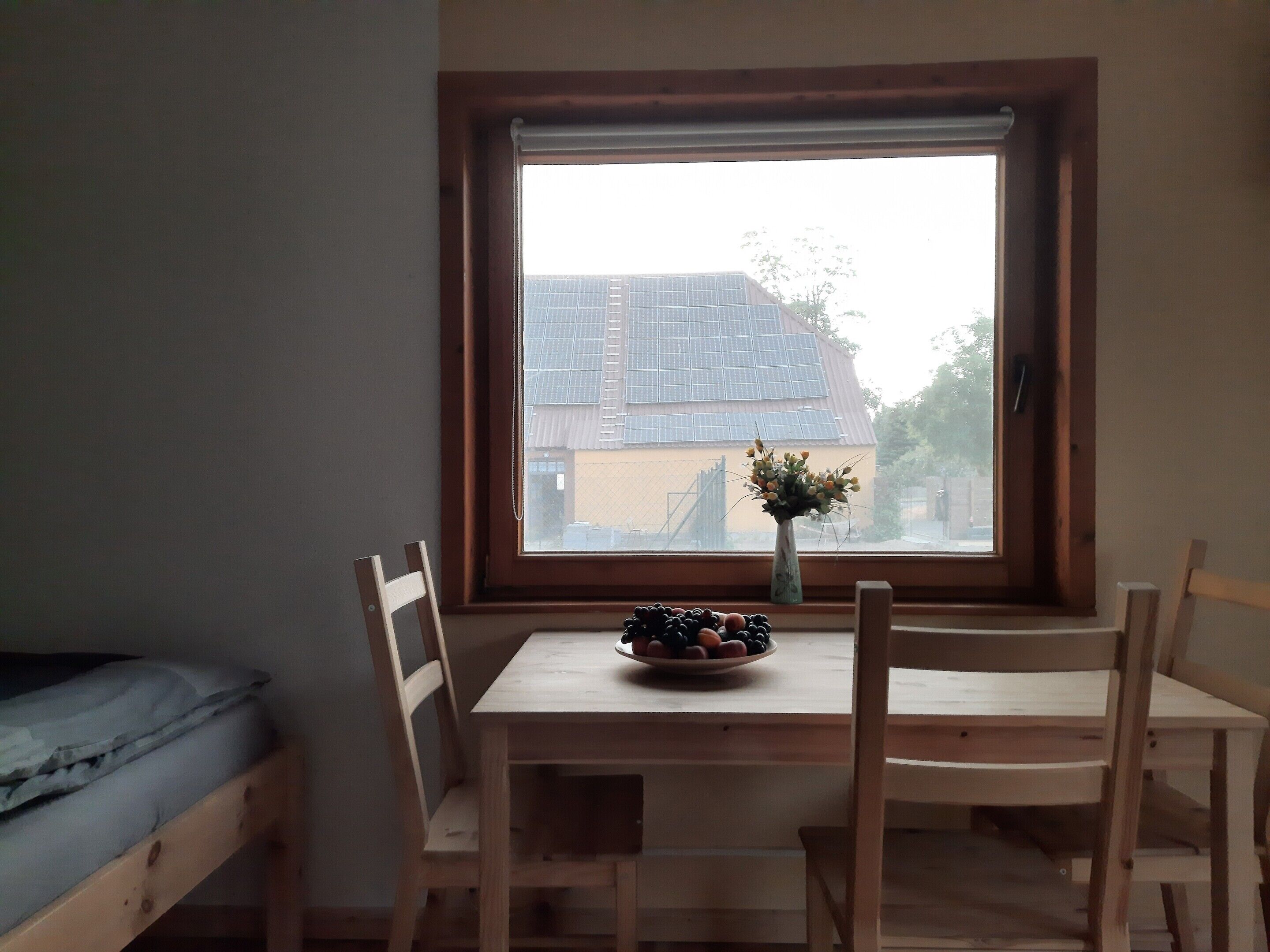 A room with a wooden table and chairs, a small window with a view of buildings, and a vase with flowers on the table.