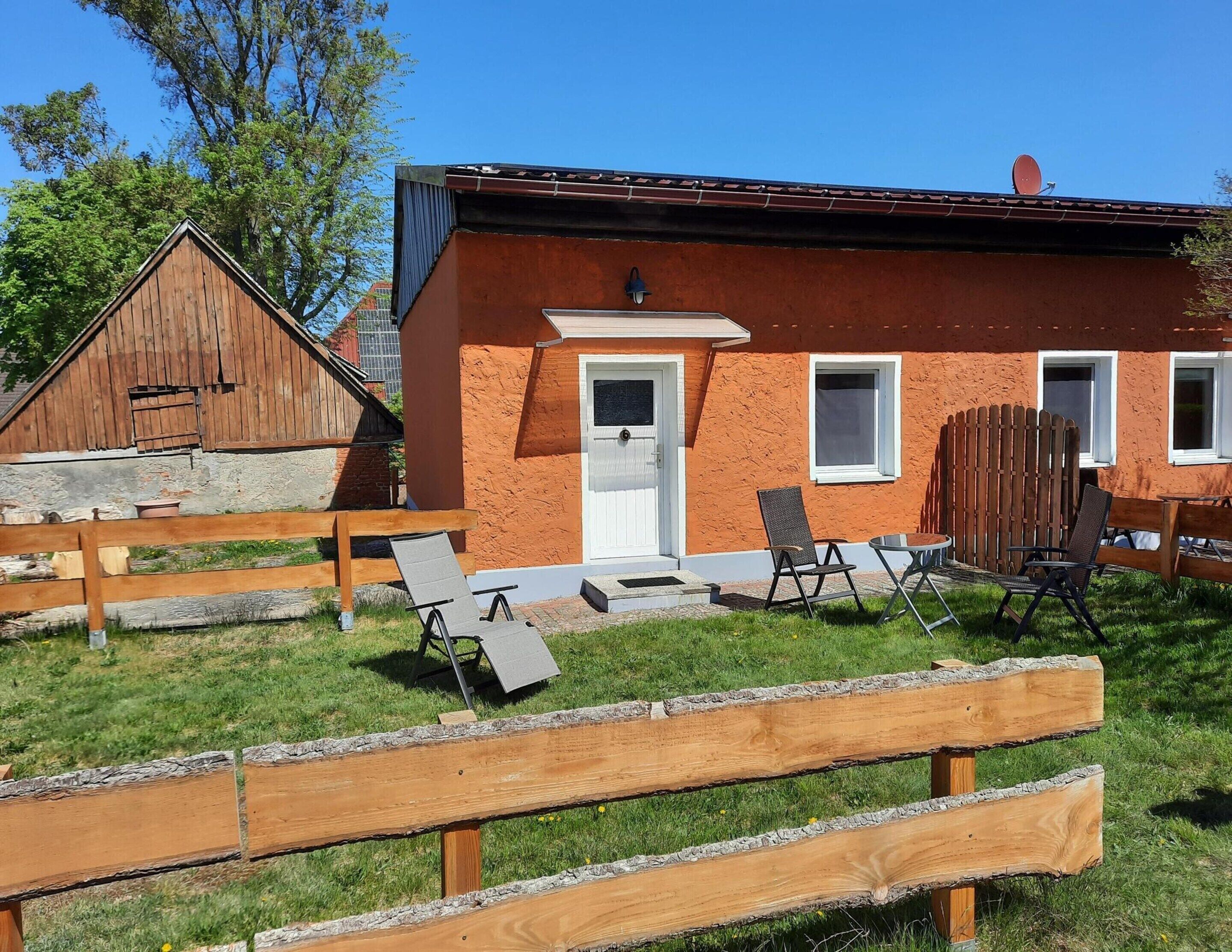 Ein rustikales Haus mit einem hölzernen Schuppen, einer kleinen Veranda mit zwei Stühlen und einem grünen Rasen.