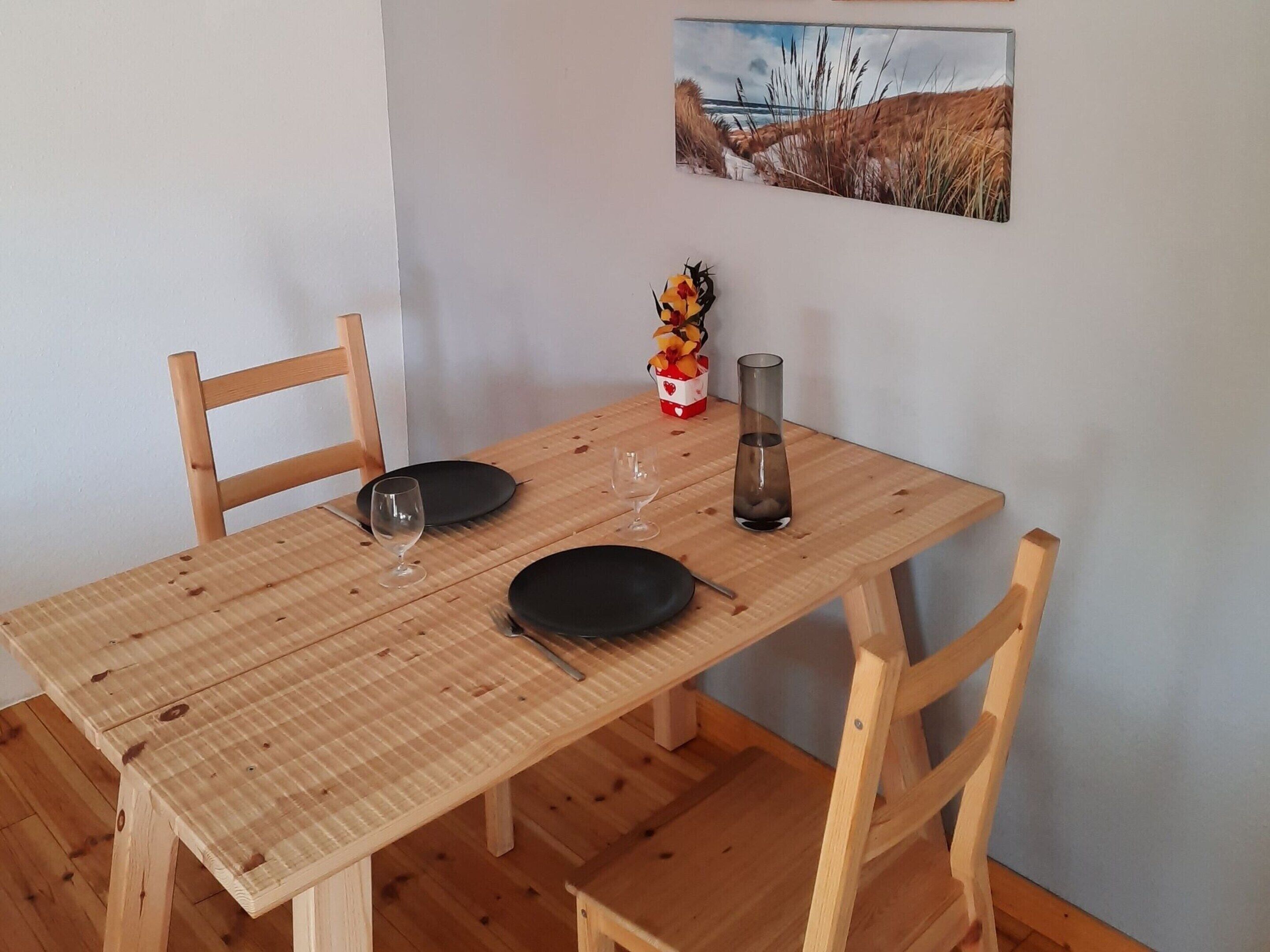 Une table de salle à manger en bois, accompagnée de deux chaises, un vase rempli de fleurs et un tableau accroché au mur.