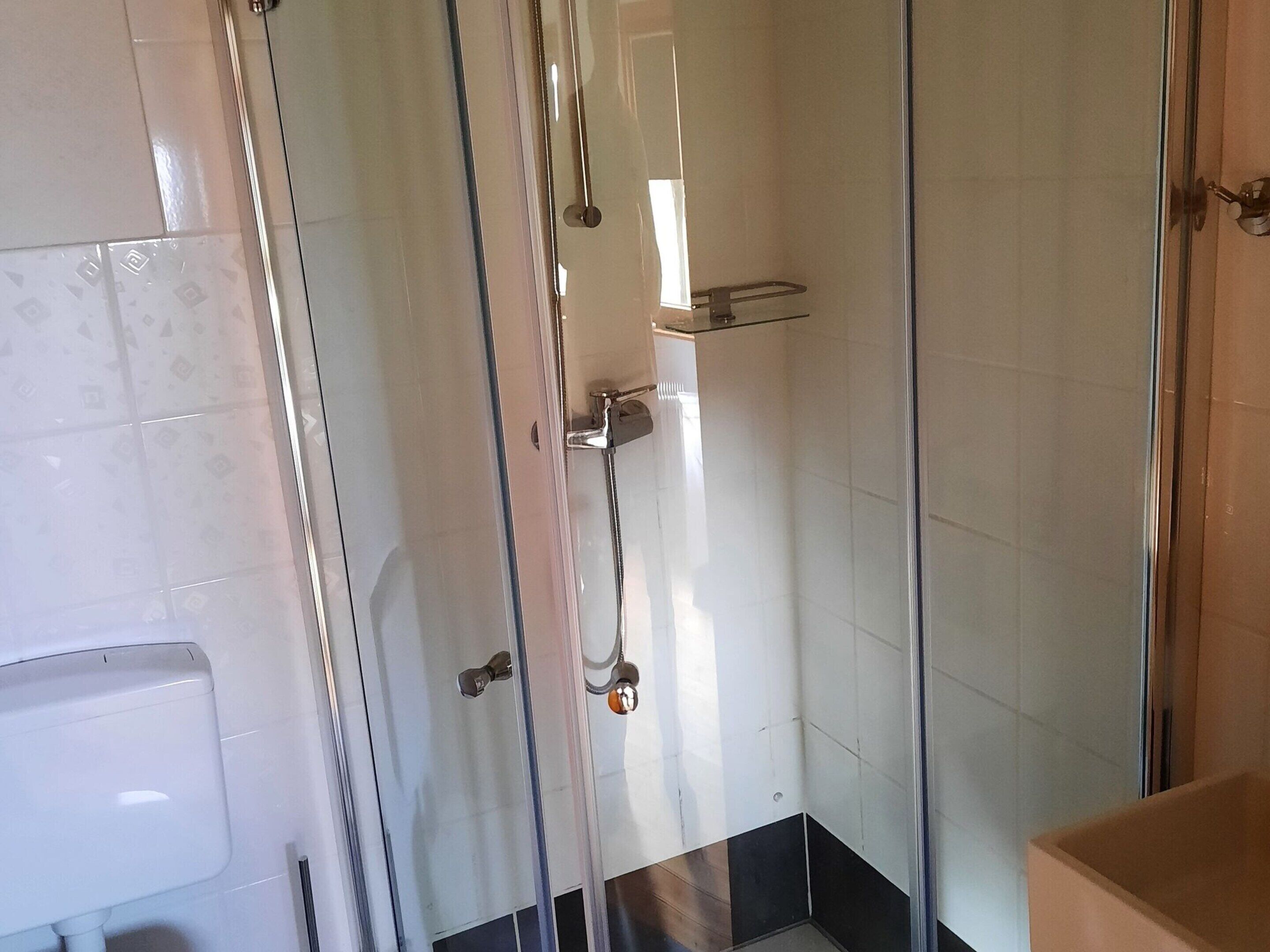A glass-enclosed shower with a chrome handle and a glass shelf.