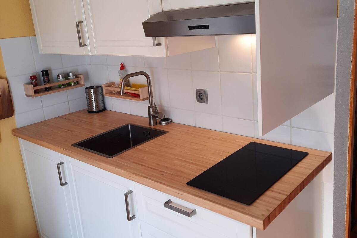 A modern kitchen with white cabinets, a stainless steel sink, and a wooden countertop.