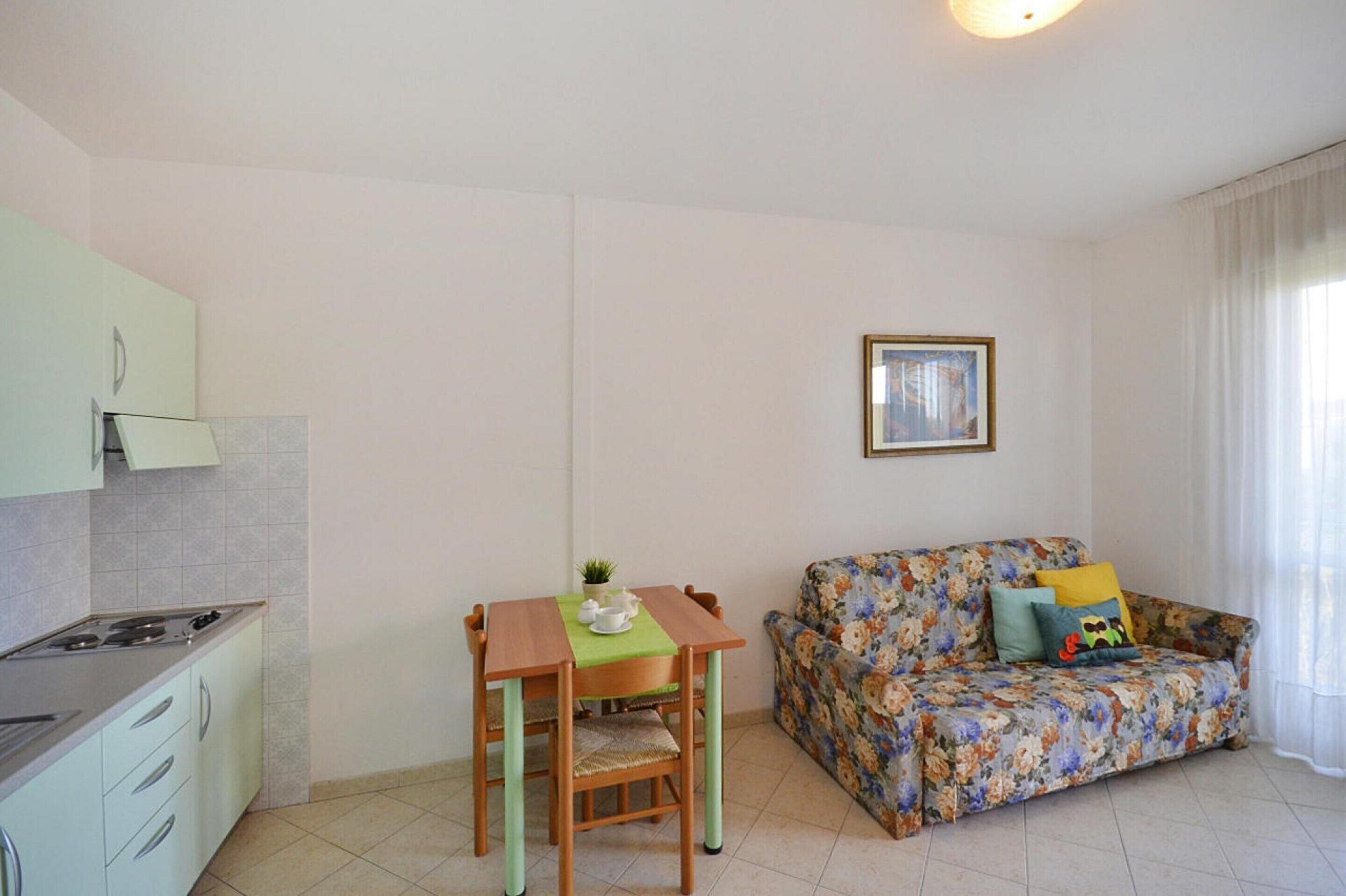 Un espai vital reduït amb zona de cuina americana, taula de dinar, sofà i un quadre al mur.