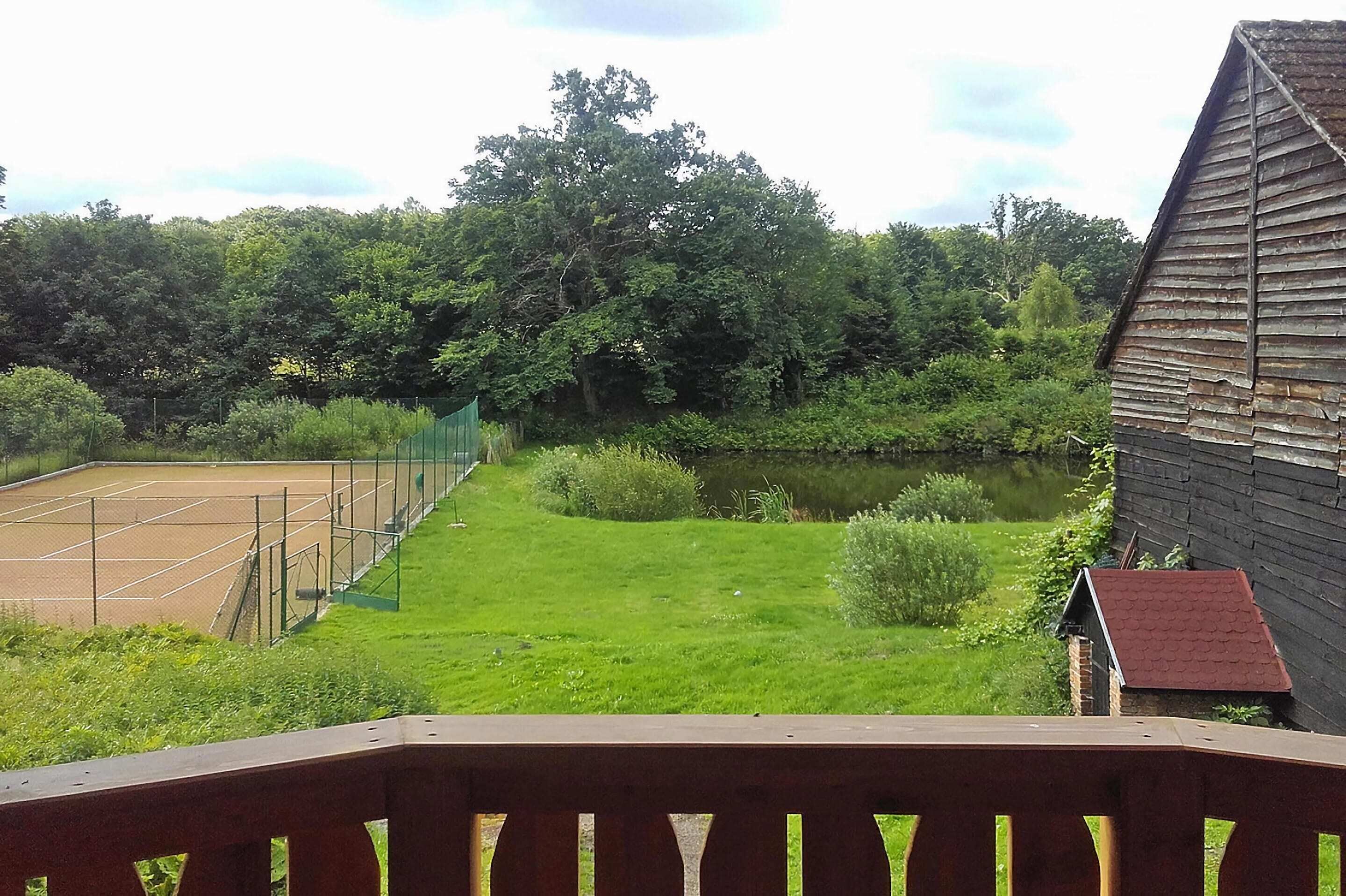 A tennis court surrounded by lush greenery and a small pond.