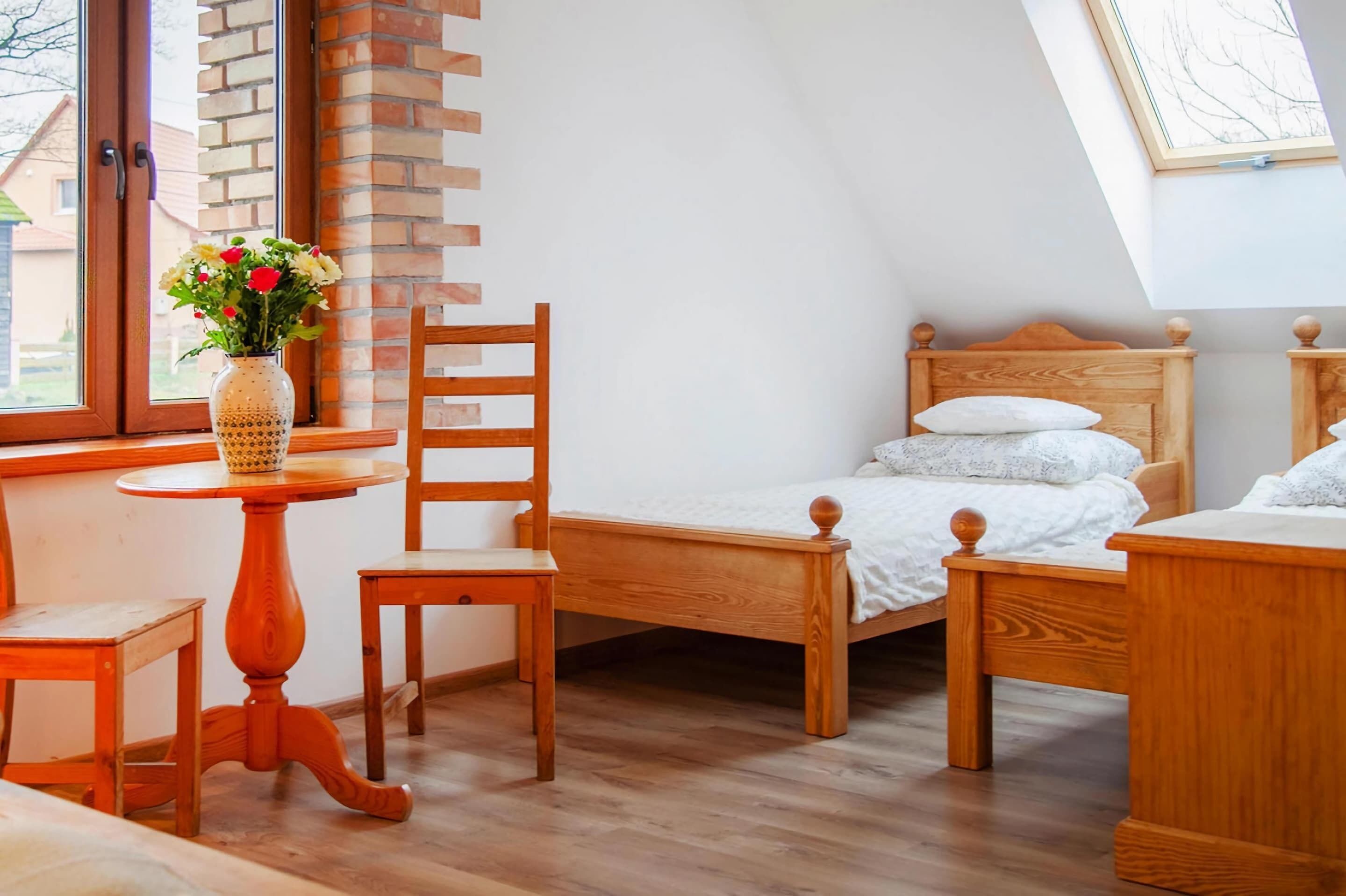 Een slaapkamer met een schuine plafond, houten meubels, een kleine tafel met een bloevas, en uitzicht buiten door een raam.